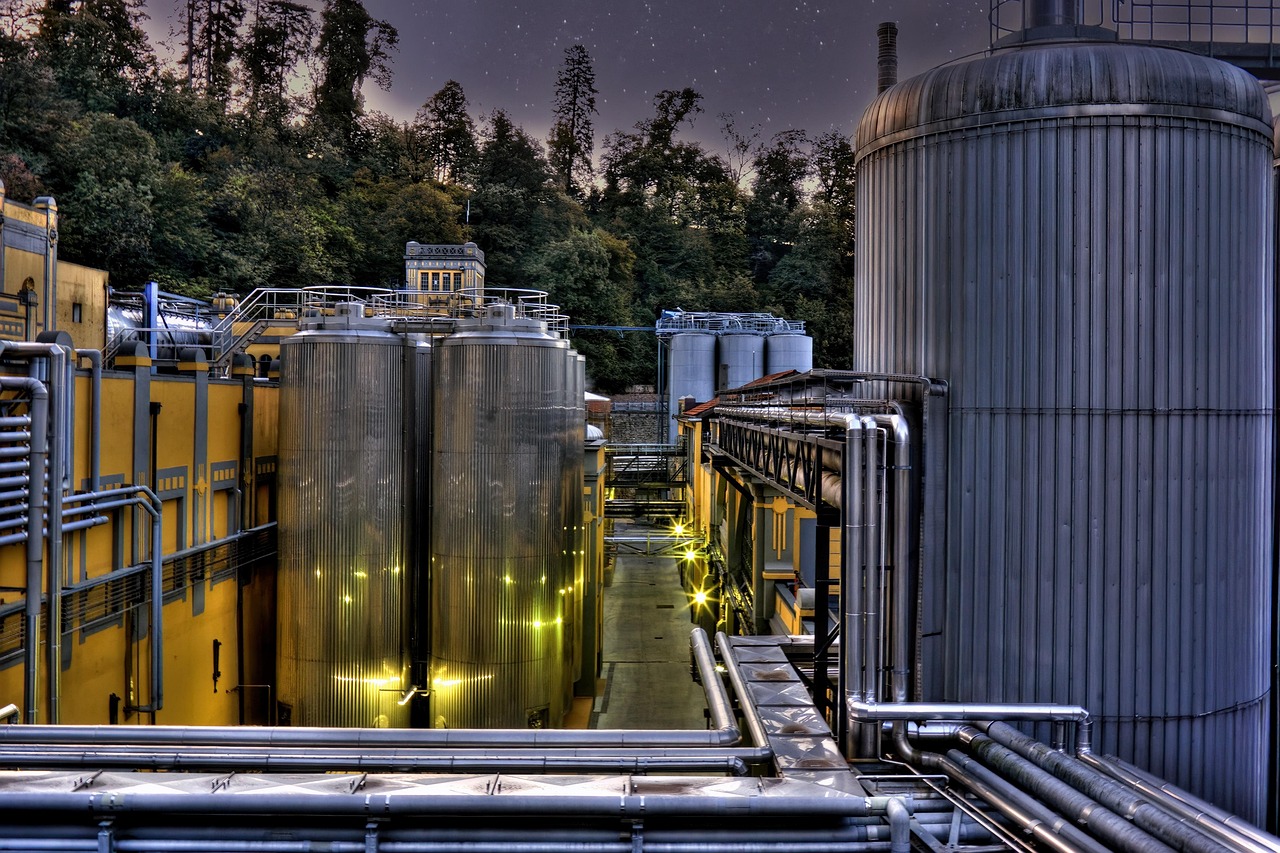 Stainless steel brewing tanks and pipework beside a yellow building at dusk