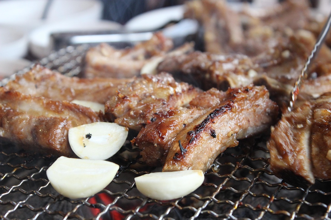 Pieces of pork ribs cooking on a wire grate with two halves of garlic in the foreground