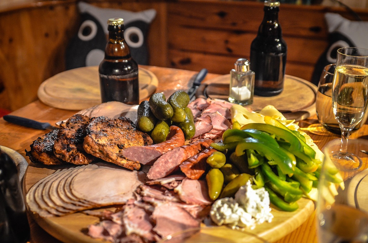 A wooden board of sliced meats, sausage, pickles and peppers