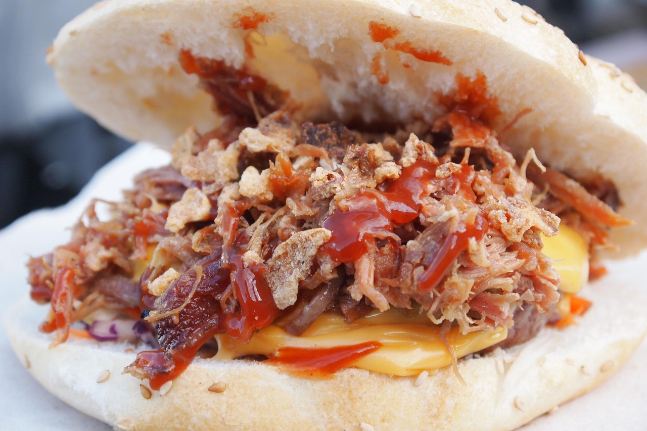A pulled pork sandwich on a toasted bun with cheese, barbecue sauce and slaw