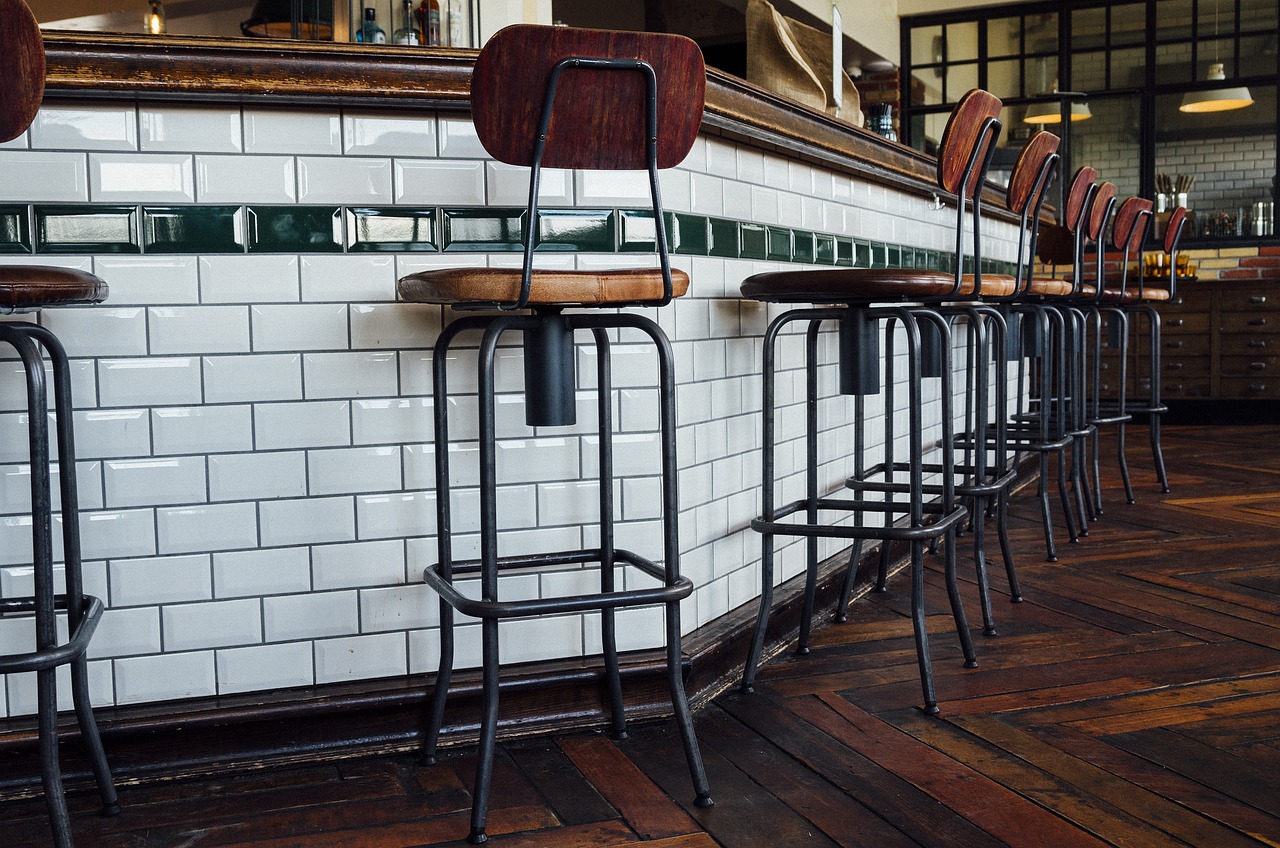 A row of tall stools with wooden seats and metal legs along a white tiled counter